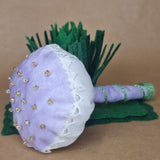 A handmade fabric mushroom prop with a lavender and white cotton head, decorated with seed beads and lace trim, attached to a lavender and green stem, displayed on a tan background.